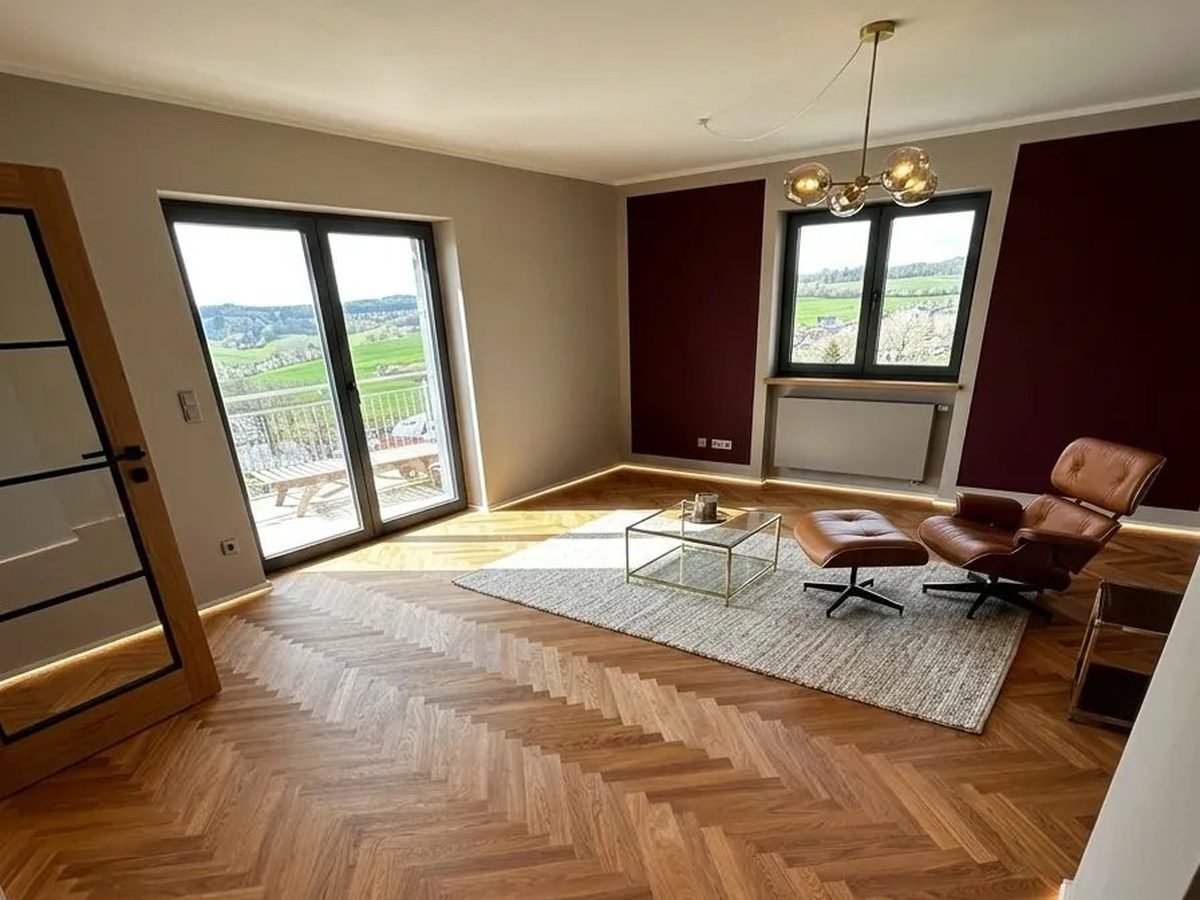 Eiche-Fischgrätparkett im Wohnzimmer mit Eames-Sessel, indirekter Beleuchtung und Blick in die Westerwald-Landschaft
